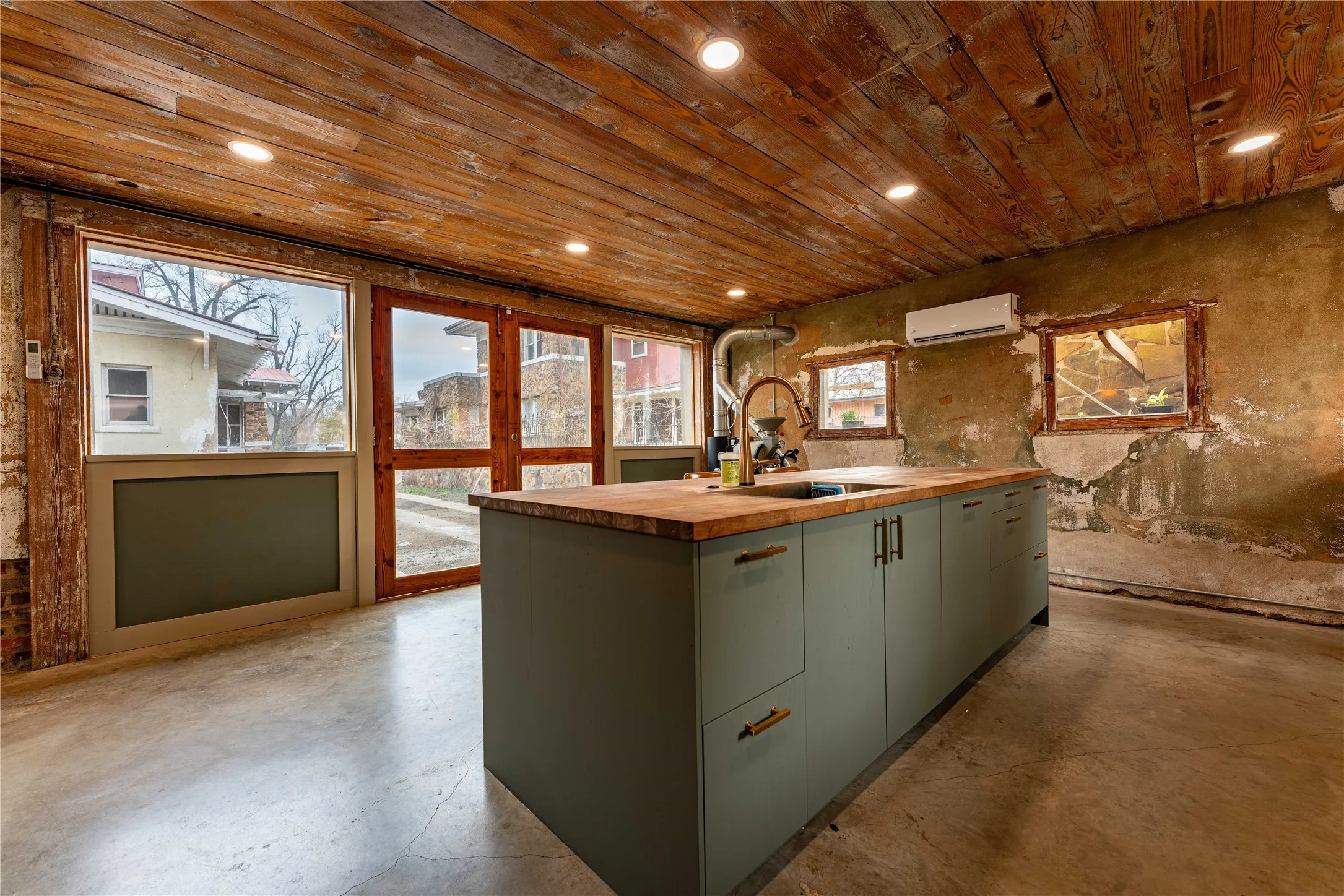 Kitchen featuring a wall unit AC, a center island with sink, a sink, finished concrete floors, and butcher block countertops