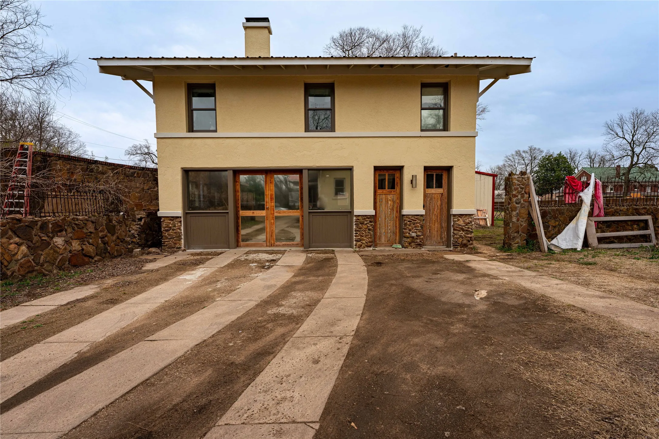 View of front of home with stucco siding, stone siding, a chimney, and fence