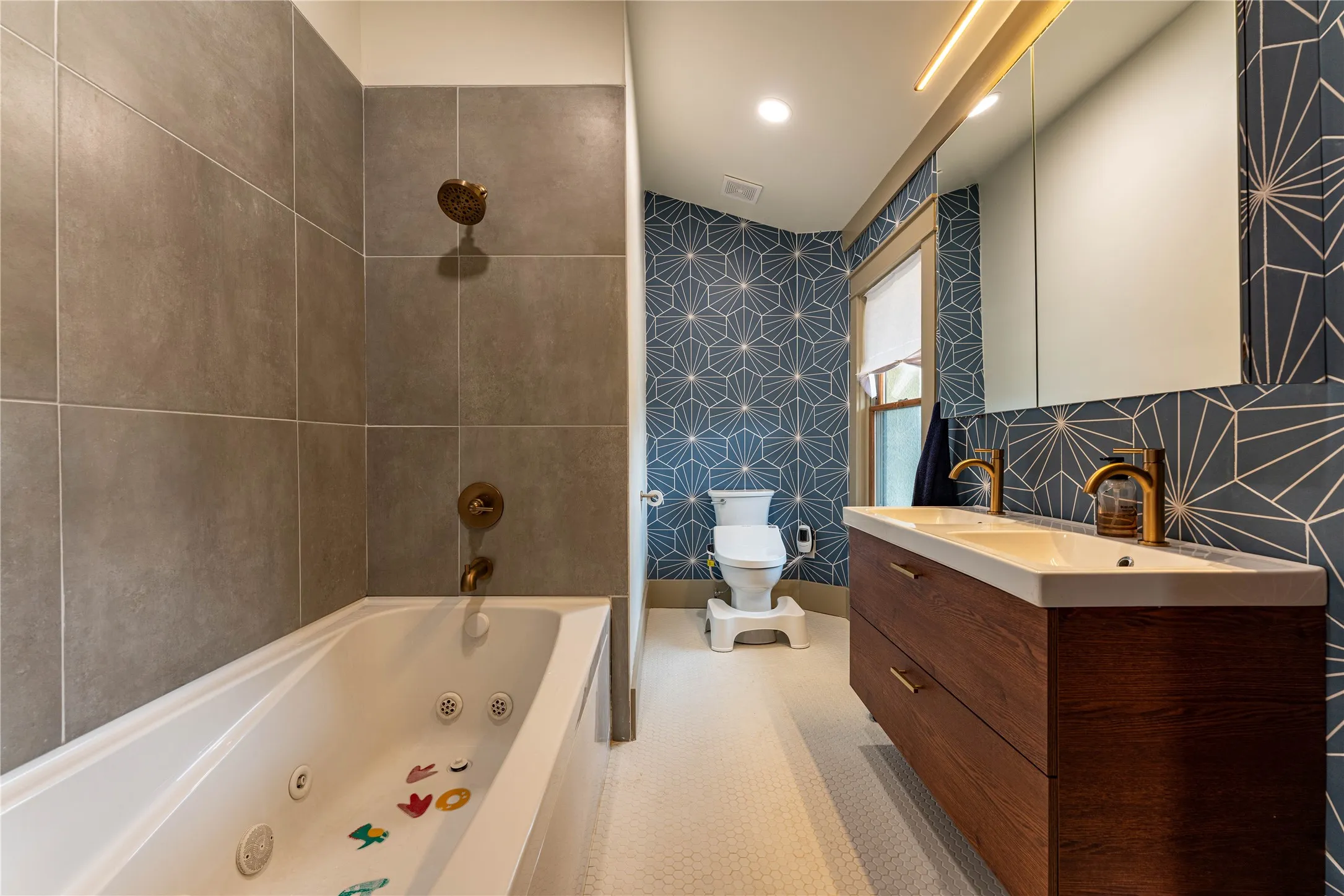Full bathroom with double vanity, toilet, a combined bath / shower with jetted tub, and a sink