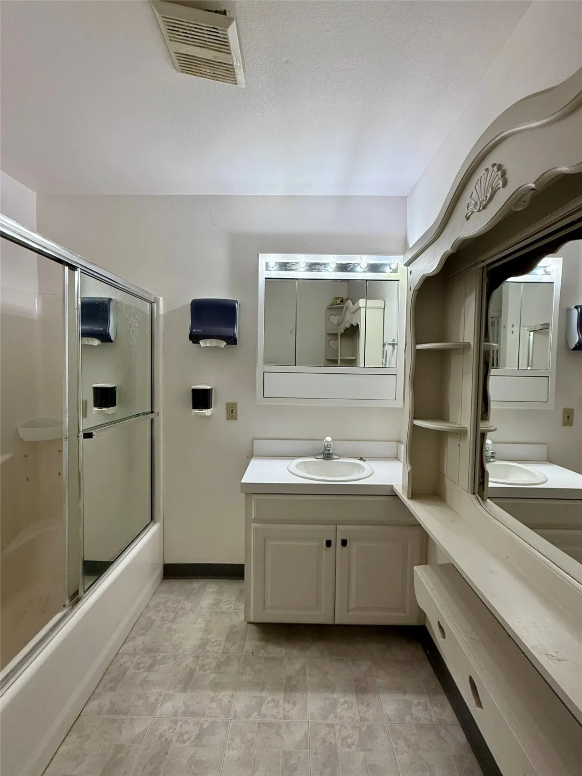 Full bathroom featuring visible vents, shower / bath combination with glass door, vanity, and a textured ceiling