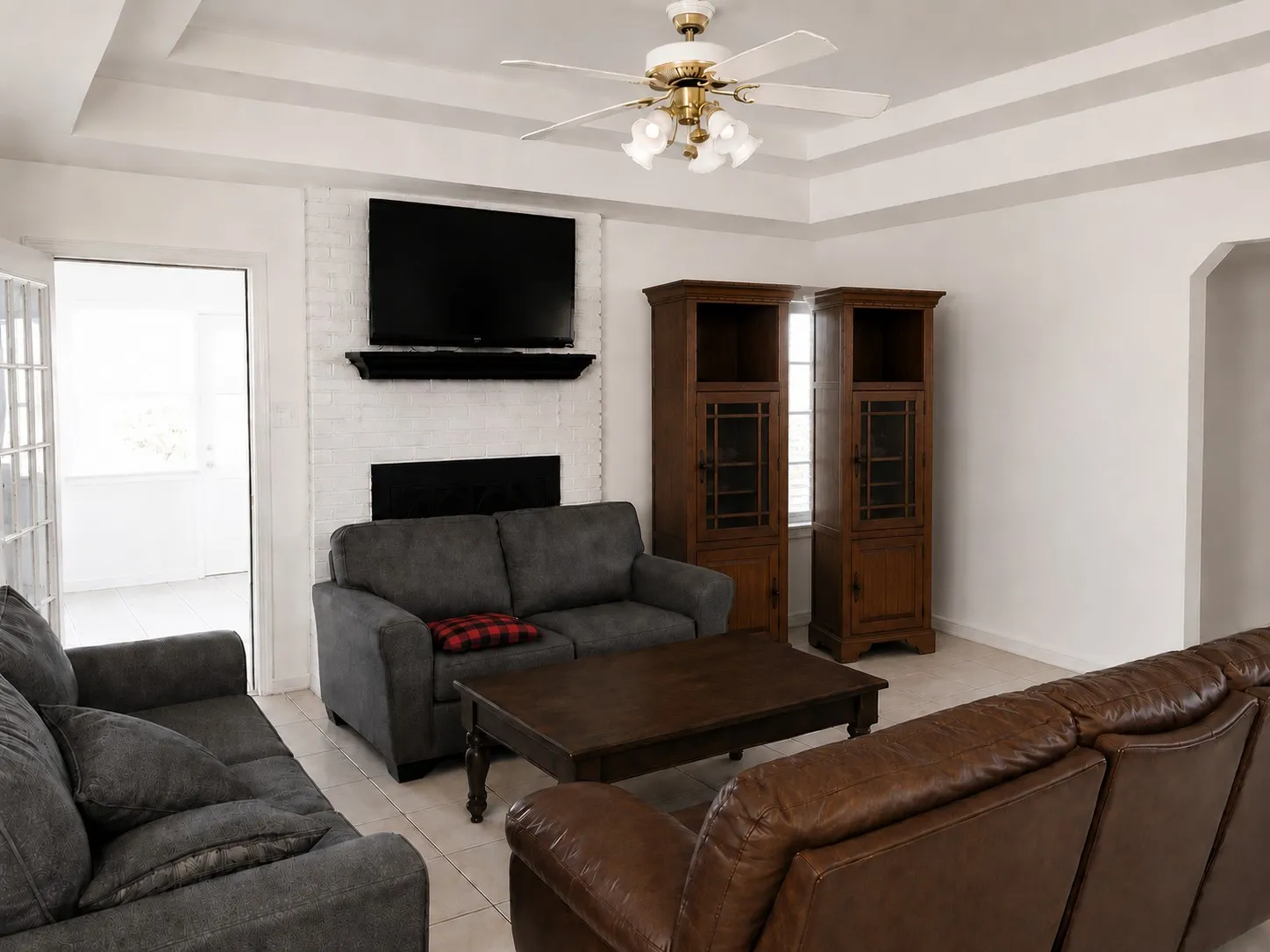 Tiled living room with a ceiling fan, a brick fireplace, and a raised ceiling