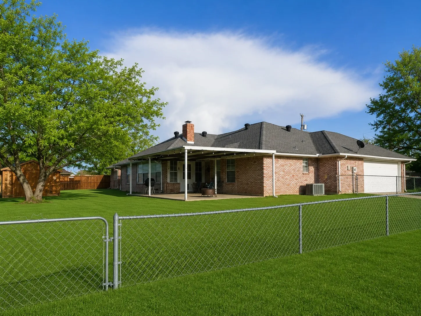 ack of house featuring a lawn, a fenced backyard, an attached garage, brick siding, and a chimney