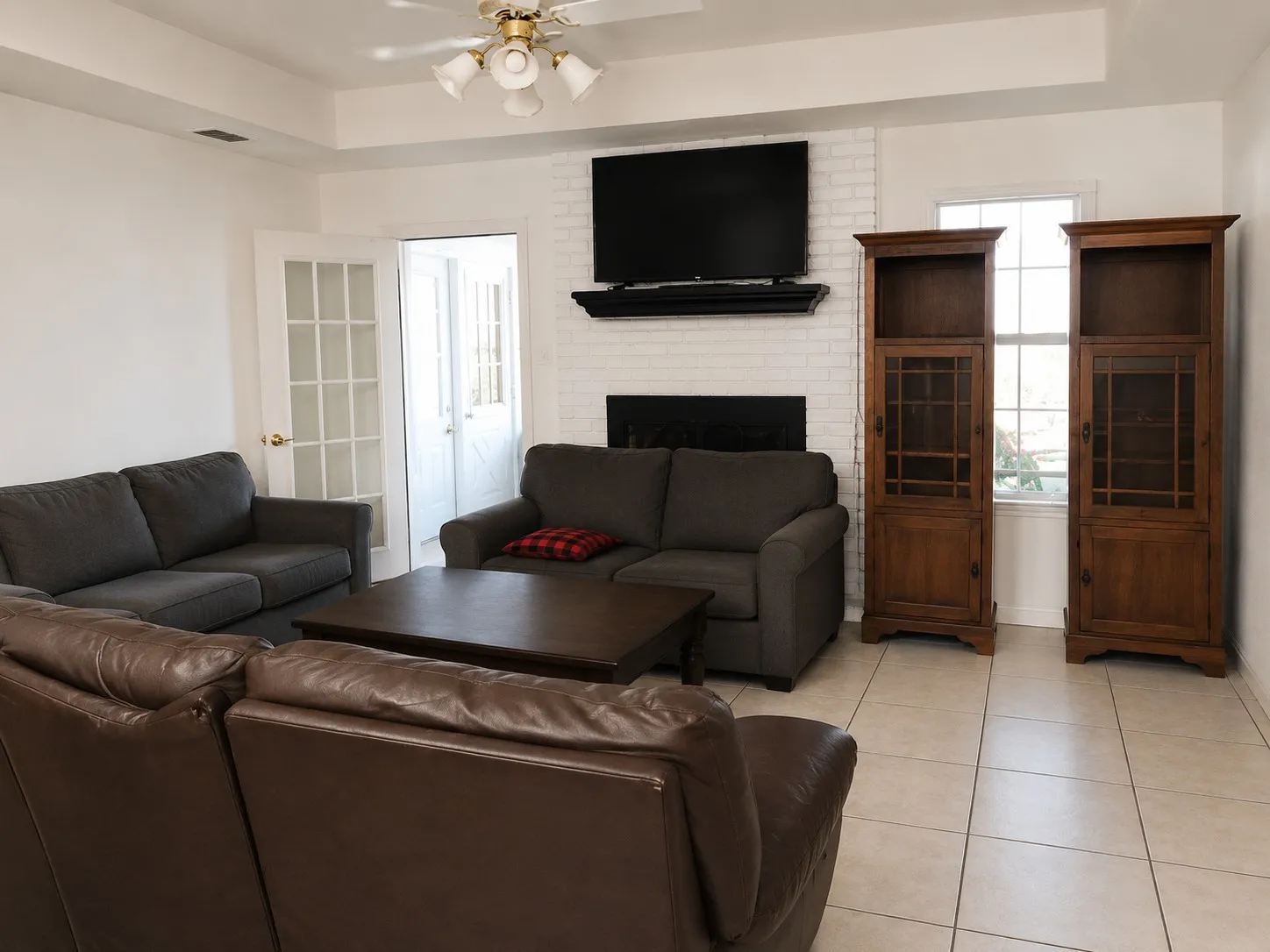 Tiled living room with a ceiling fan, a brick fireplace, and a raised ceiling