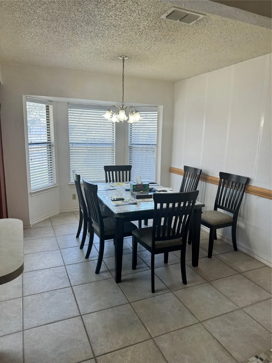 Dining room featuring a textured ceiling, light tile patterned floors, baseboards, visible vents, and an inviting chandelier