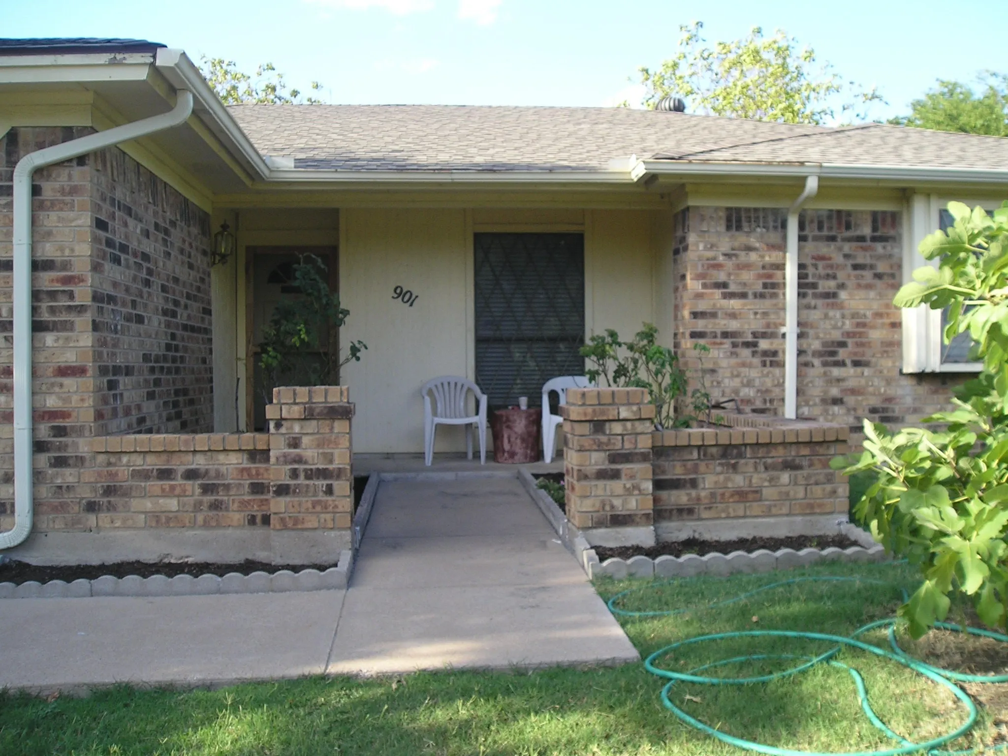 Doorway to property featuring a shingled roof, covered porch, and brick siding