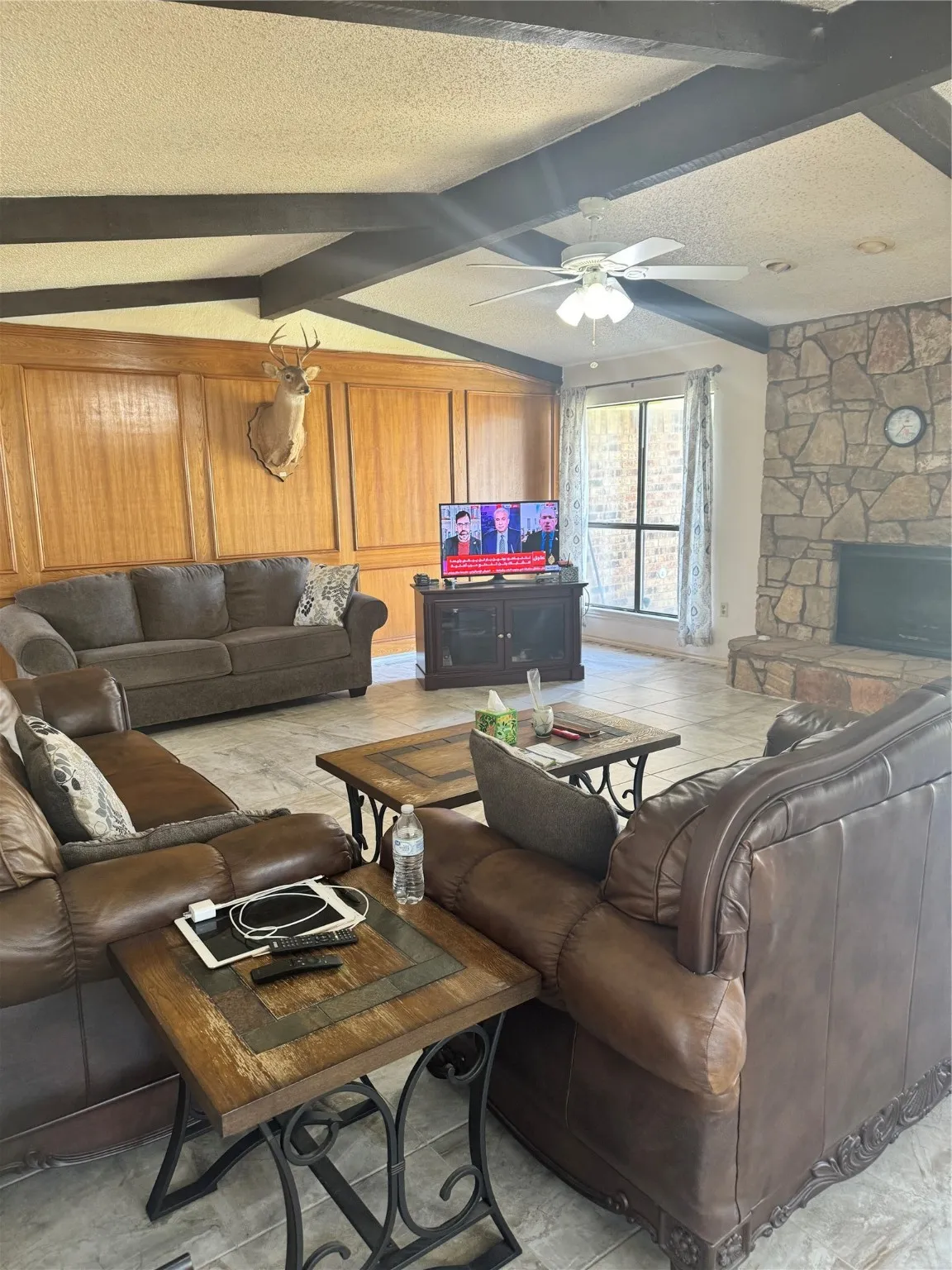 Living area featuring a fireplace, beamed ceiling, ceiling fan, and a textured ceiling