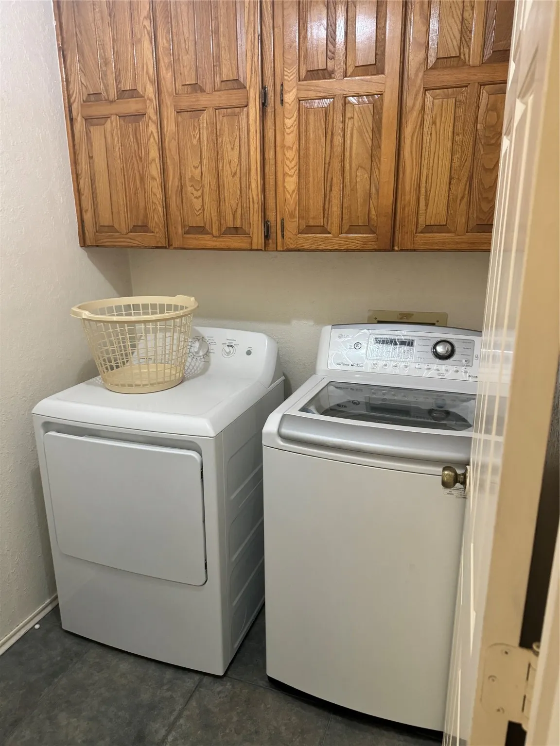 Laundry room with independent washer and dryer, cabinet space, dark tile patterned flooring, and a textured wall