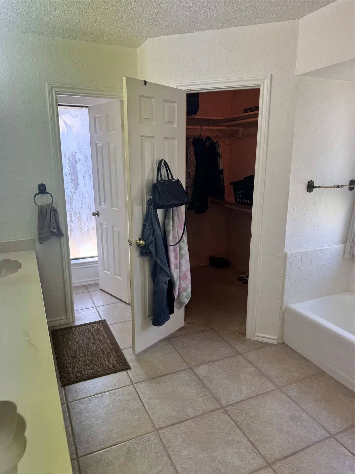 Full bath featuring a textured ceiling, a bathtub, tile patterned floors, a textured wall, and a walk in closet