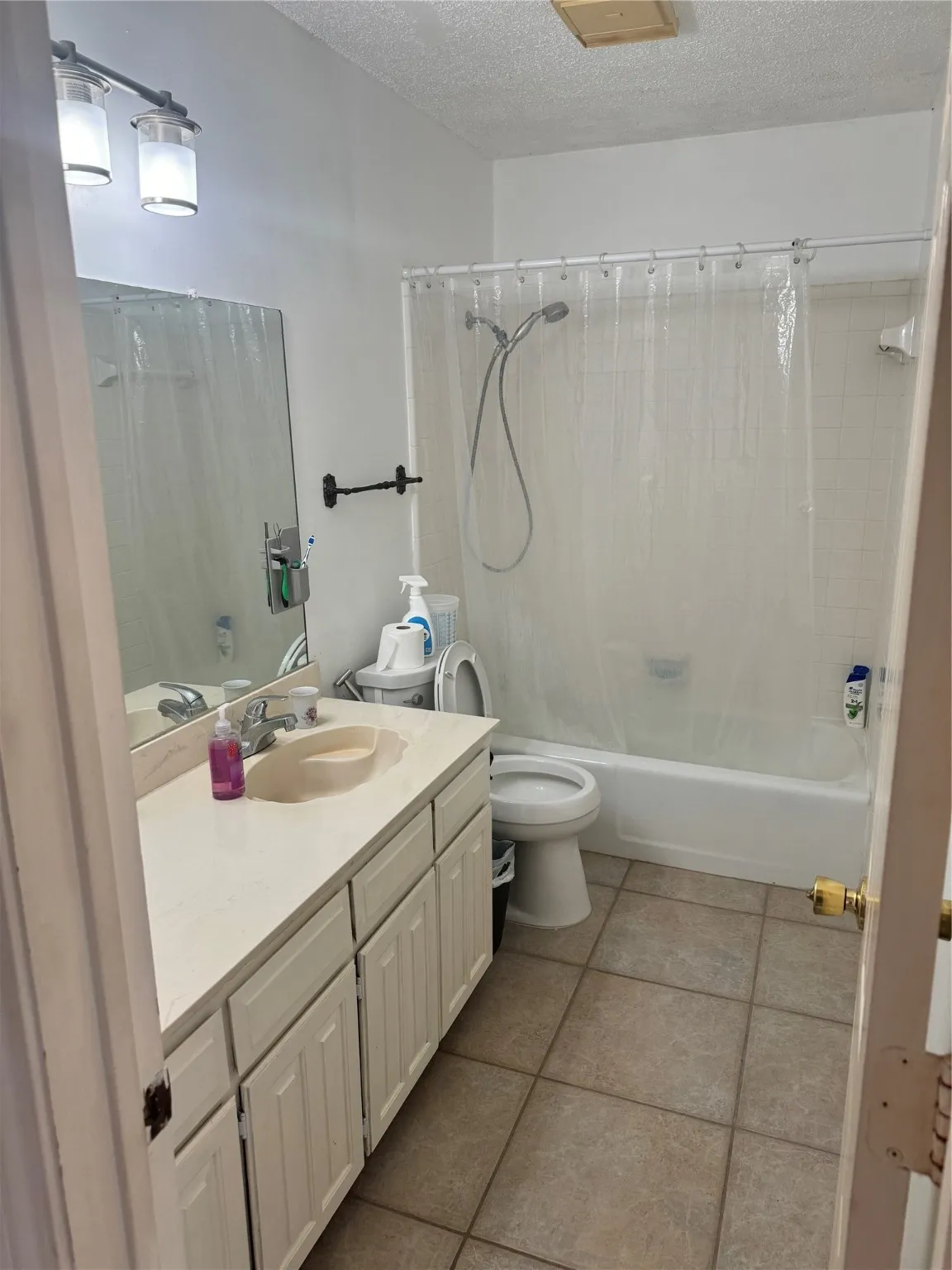 Bathroom featuring tile patterned floors, toilet, vanity, shower / bath combo, and a textured ceiling