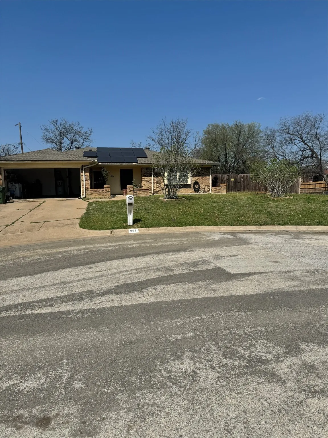 View of front of house featuring concrete driveway, fence, a front lawn, roof mounted solar panels, and a carport