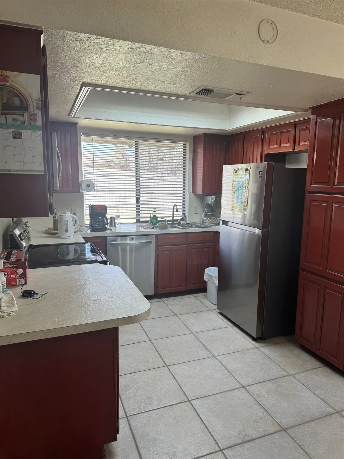 Kitchen featuring range, a textured ceiling, dark brown cabinets, dishwashing machine, and fridge