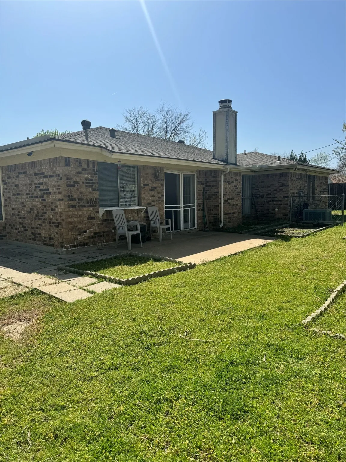 Back of property with a chimney, a patio, brick siding, and a yard