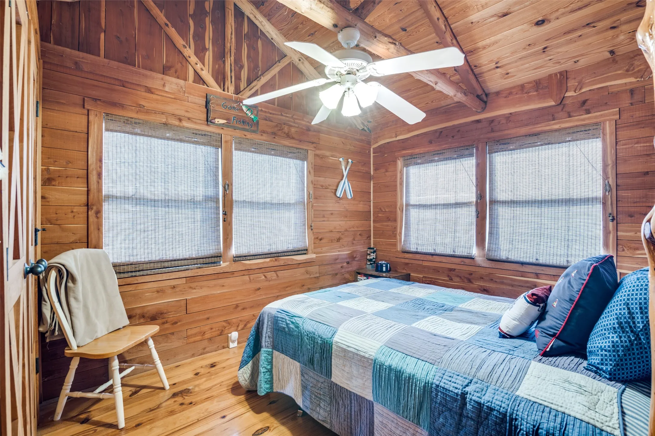 Bedroom featuring wooden ceiling, a ceiling fan, wooden walls, beamed ceiling, and hardwood floors