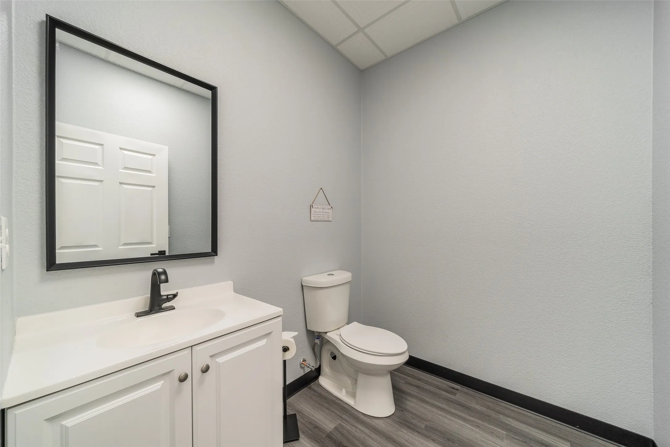 Half bath with vanity, toilet, baseboards, a drop ceiling, and wood finished floors