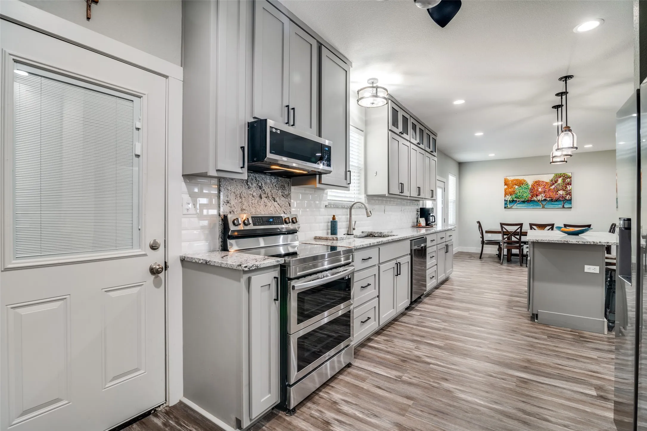 Kitchen featuring custom gray cabinetry, light wood-style flooring, and double - oven, all appliances with stainless steel finishes