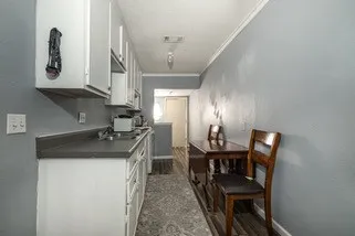 Kitchen with baseboards, ornamental molding, white cabinetry, dark countertops, and visible vents
