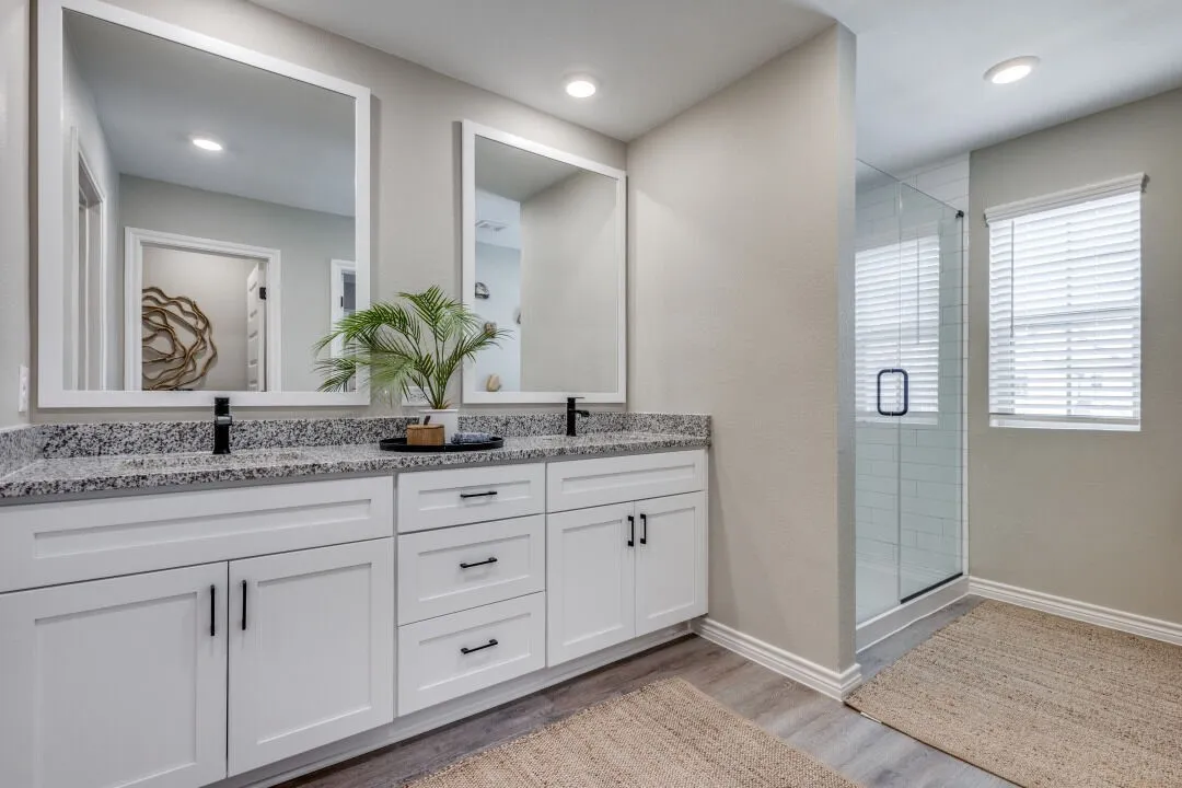 Full bath with baseboards, a sink, a stall shower, double vanity, and wood finished floors