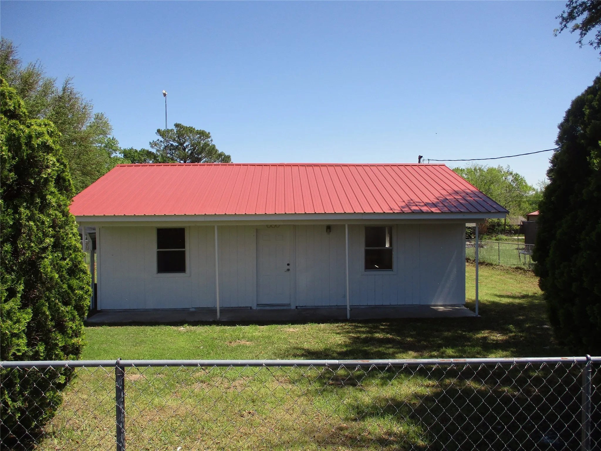 Rear view of house with metal roof, fence, and a lawn