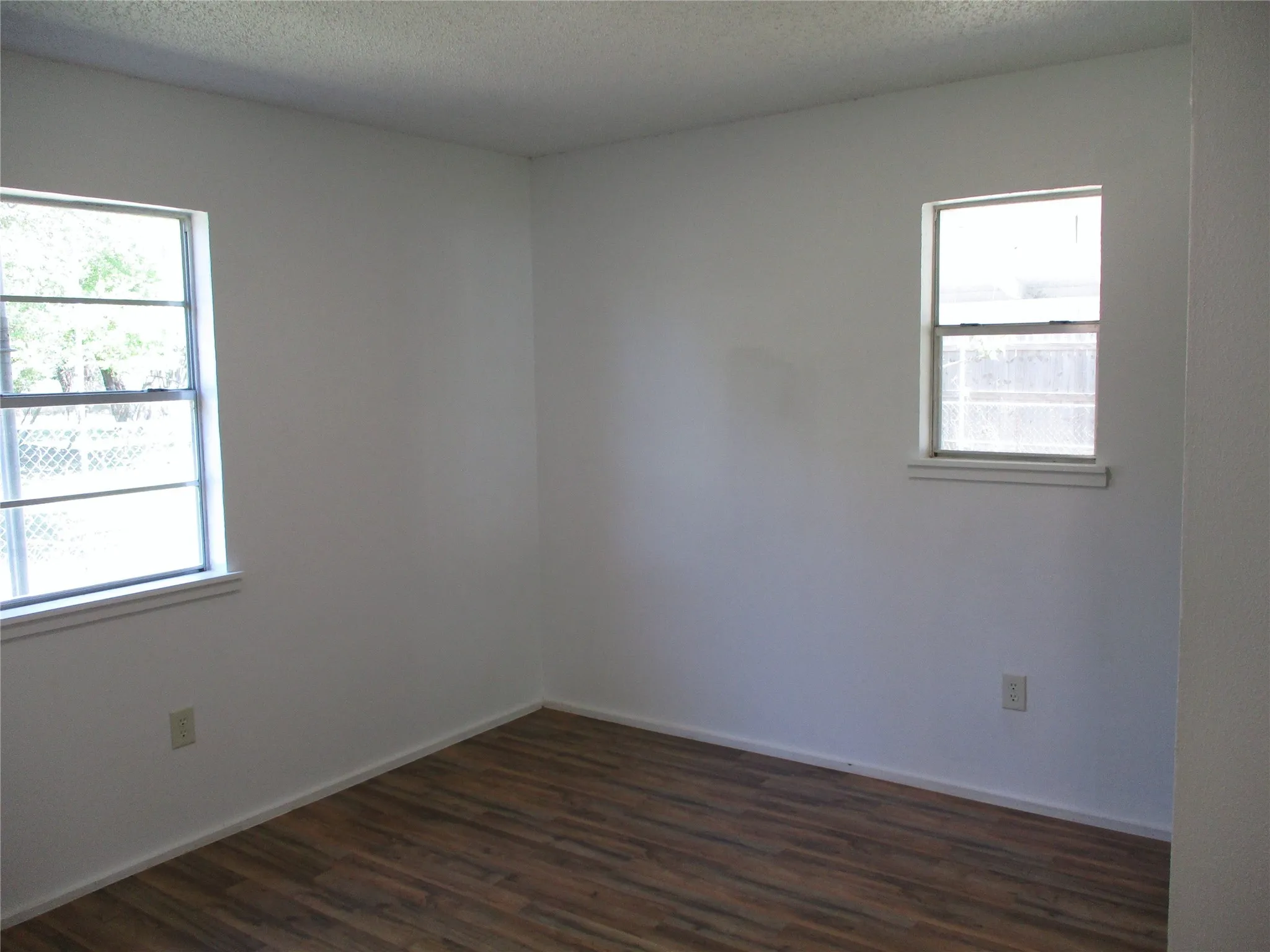 Spare room with a wealth of natural light, dark wood-type flooring, a textured ceiling, and baseboards