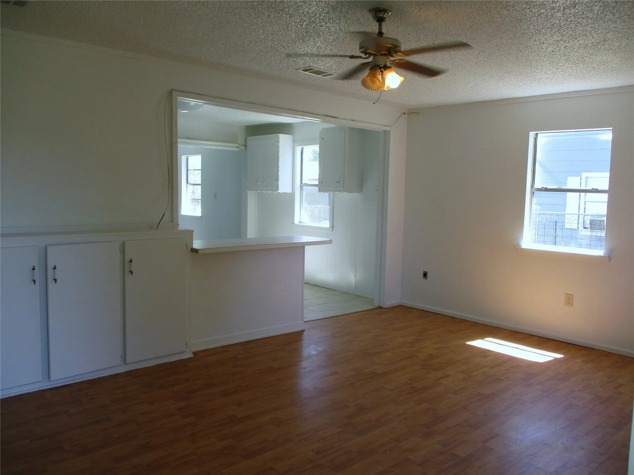 Unfurnished room with a textured ceiling, wood finished floors, a ceiling fan, and visible vents