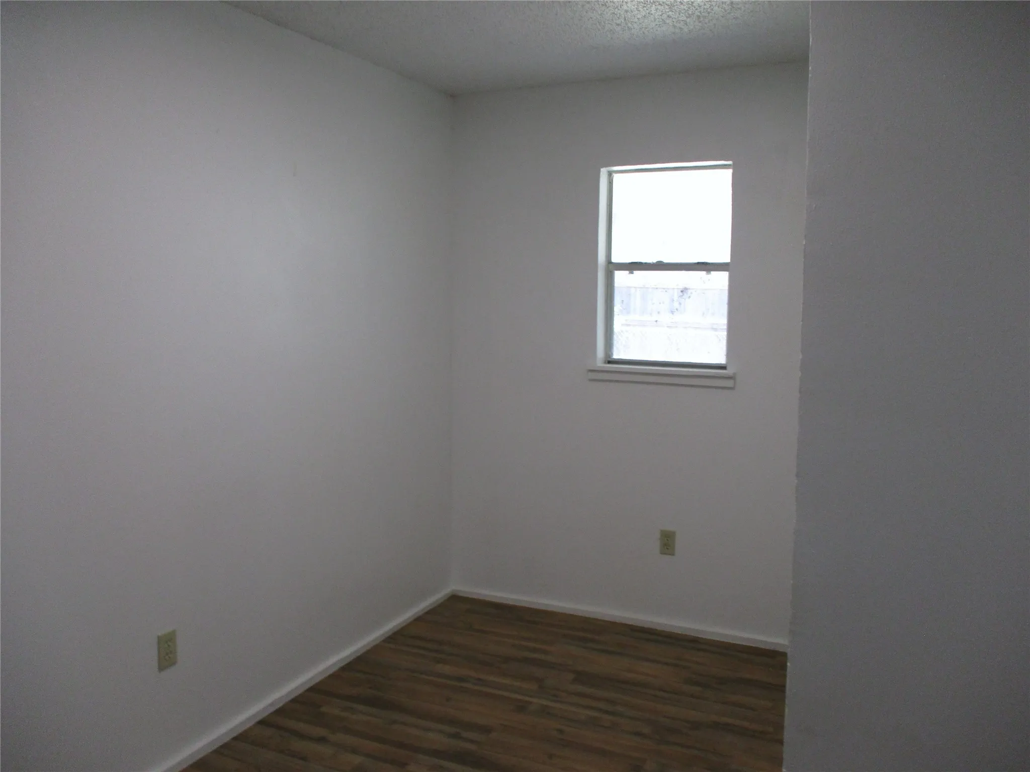 Unfurnished room with a textured ceiling, baseboards, and dark wood-style floors