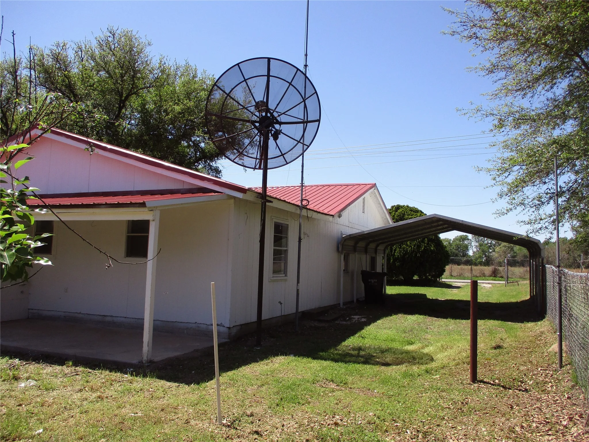 View of side of property featuring a lawn, a detached carport, a patio, metal roof, and fence