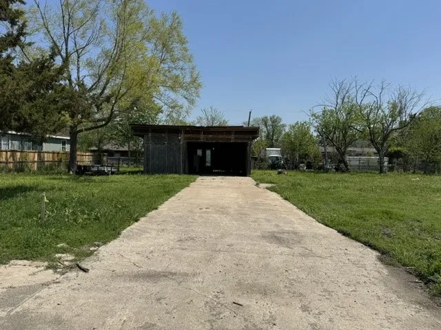 View of outdoor structure with a carport, fence, driveway, and an outbuilding