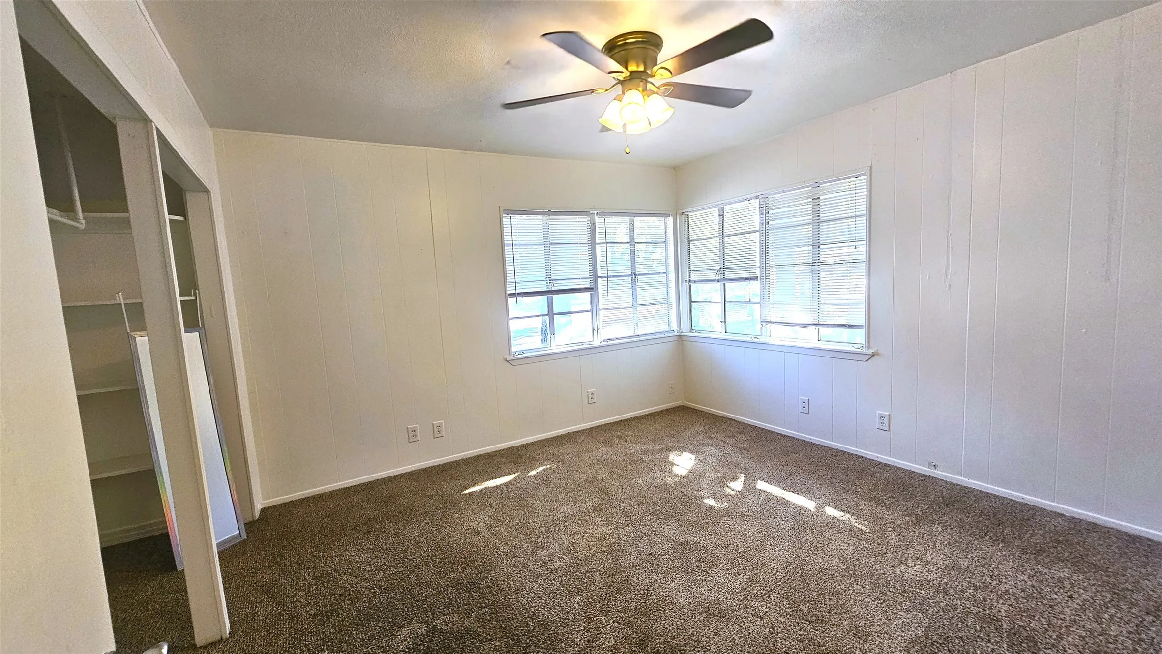 Carpeted spare room with wooden walls, a textured ceiling, and ceiling fan