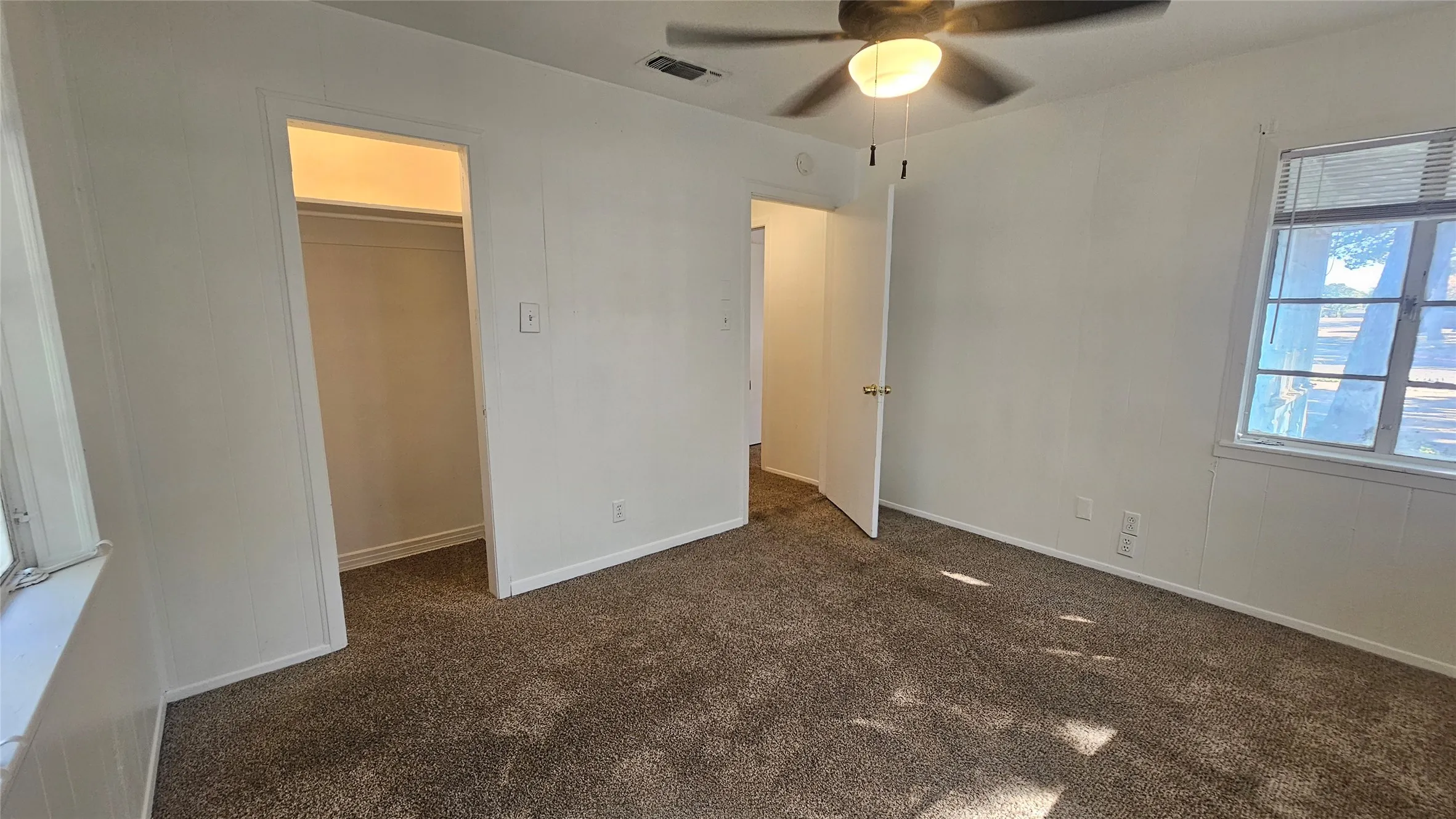 Unfurnished bedroom featuring dark carpet, a walk in closet, and ceiling fan