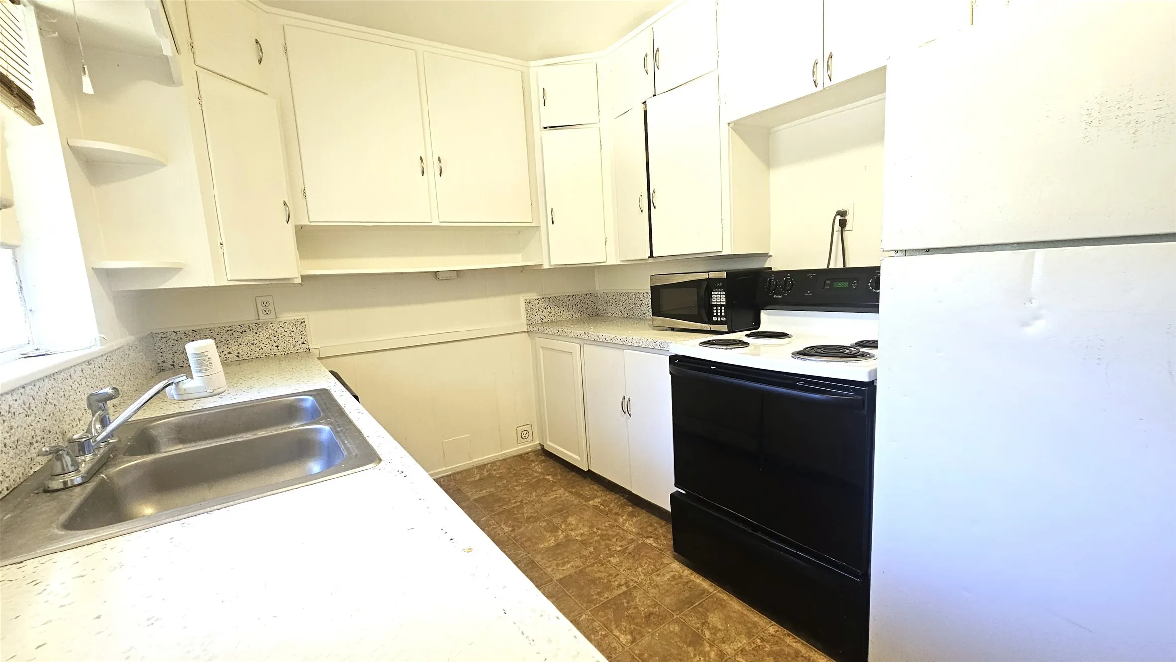 Kitchen with freestanding refrigerator, open shelves, electric range, light countertops, and white cabinets