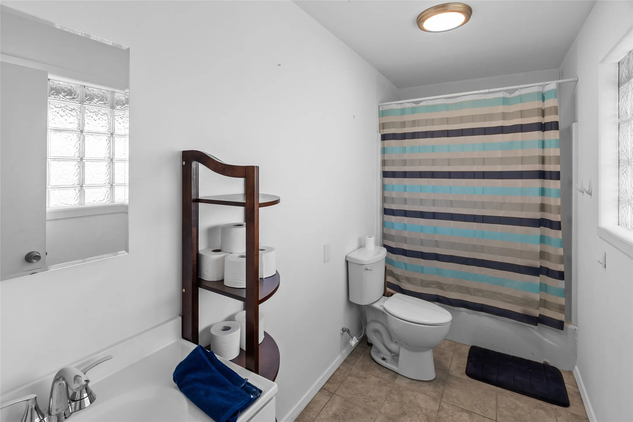 Full bath with shower / tub combo, baseboards, tile patterned flooring, toilet, and a sink