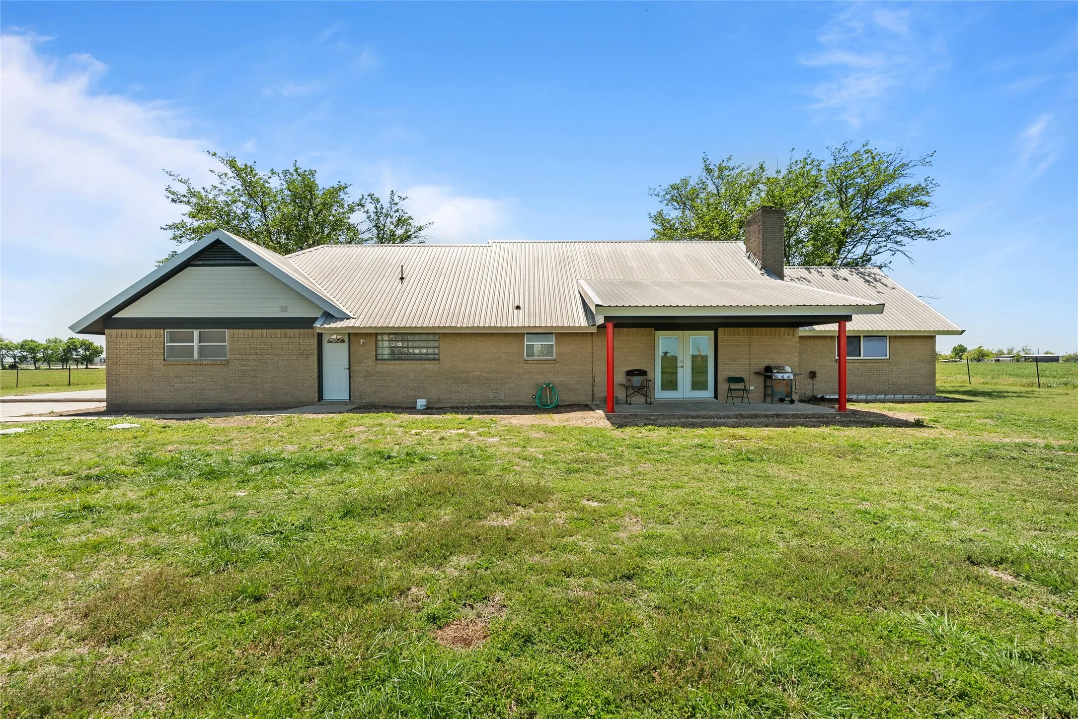 Back of house featuring a patio, french doors, brick siding, metal roof, and a lawn