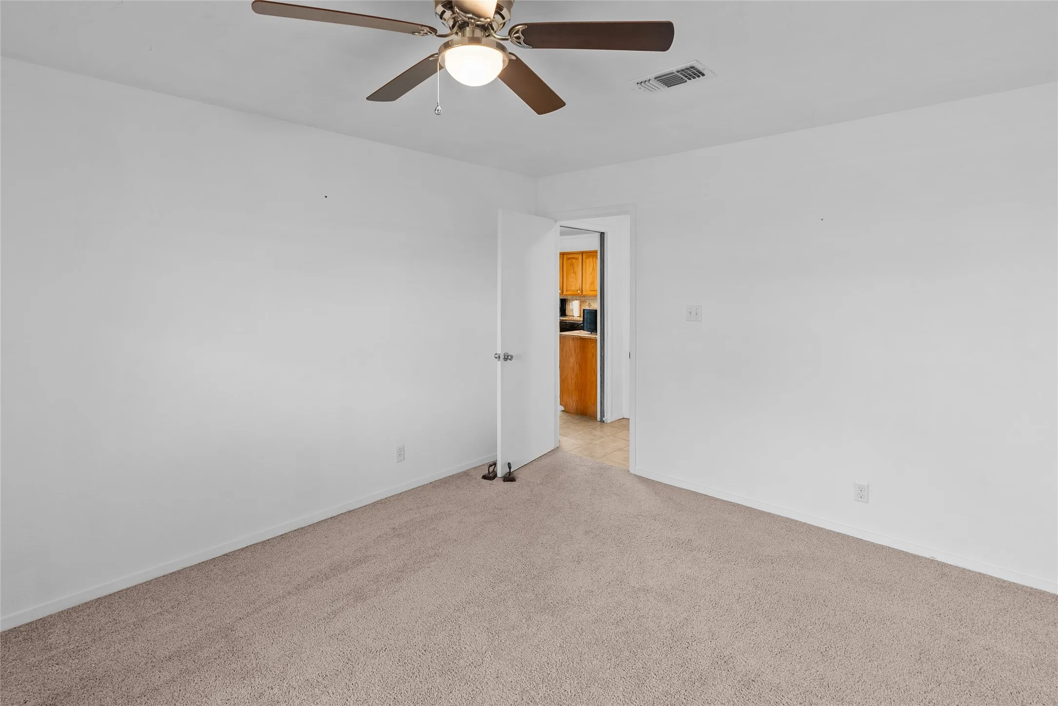 Unfurnished room featuring visible vents, light colored carpet, baseboards, and ceiling fan