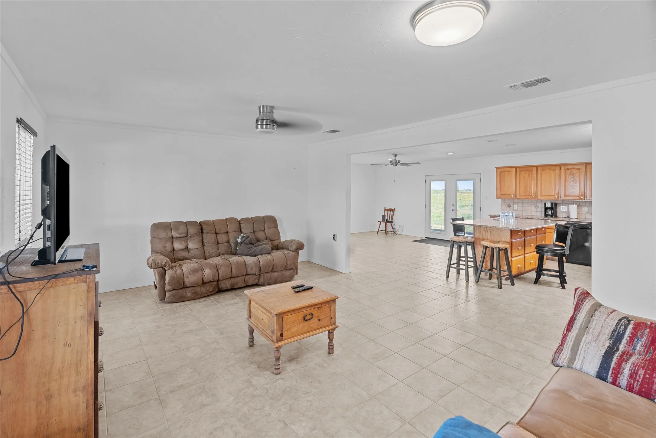 Living room featuring ornamental molding, visible vents, a ceiling fan, and light tile patterned floors