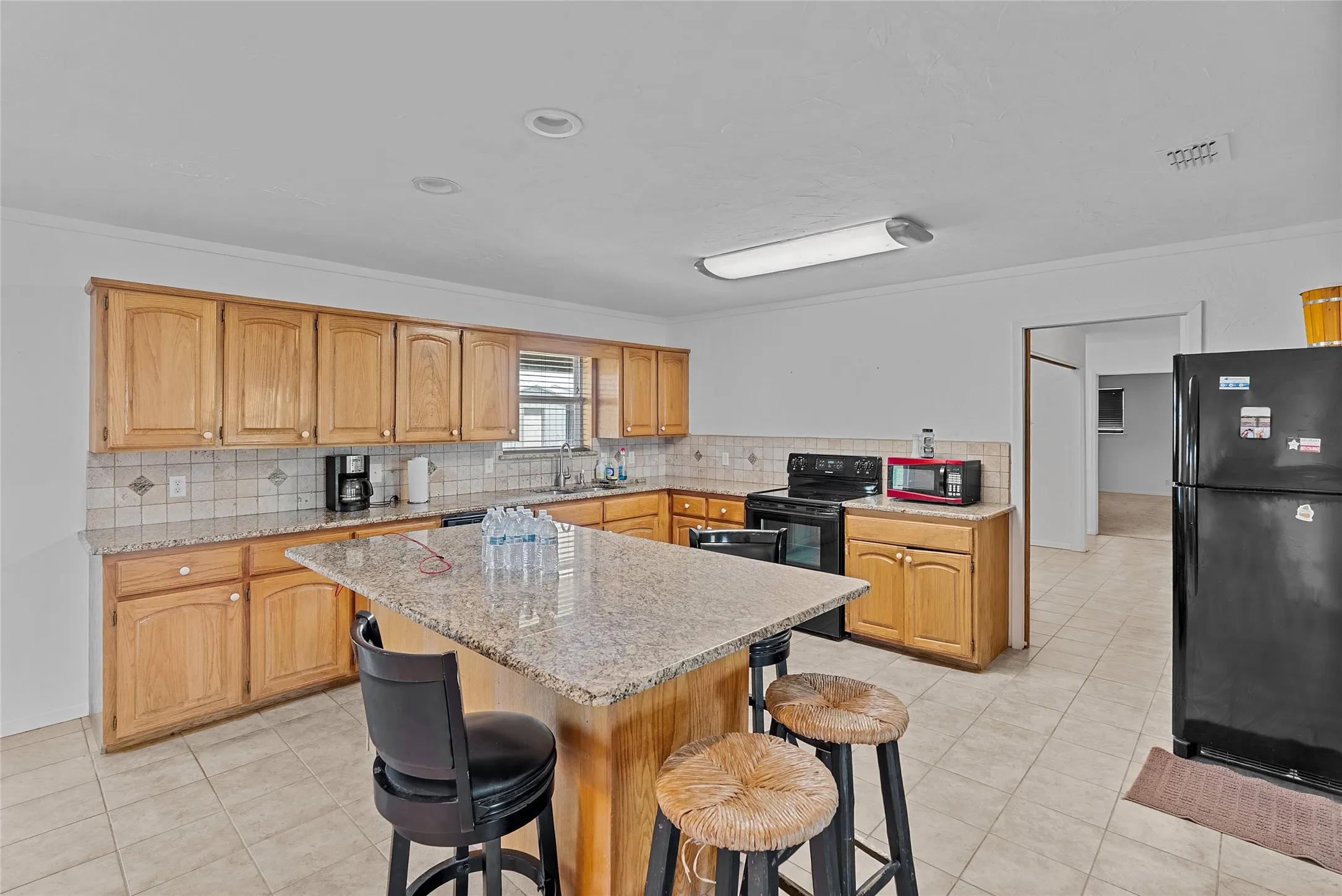 Kitchen featuring a breakfast bar area, light tile patterned flooring, a sink, and black appliances