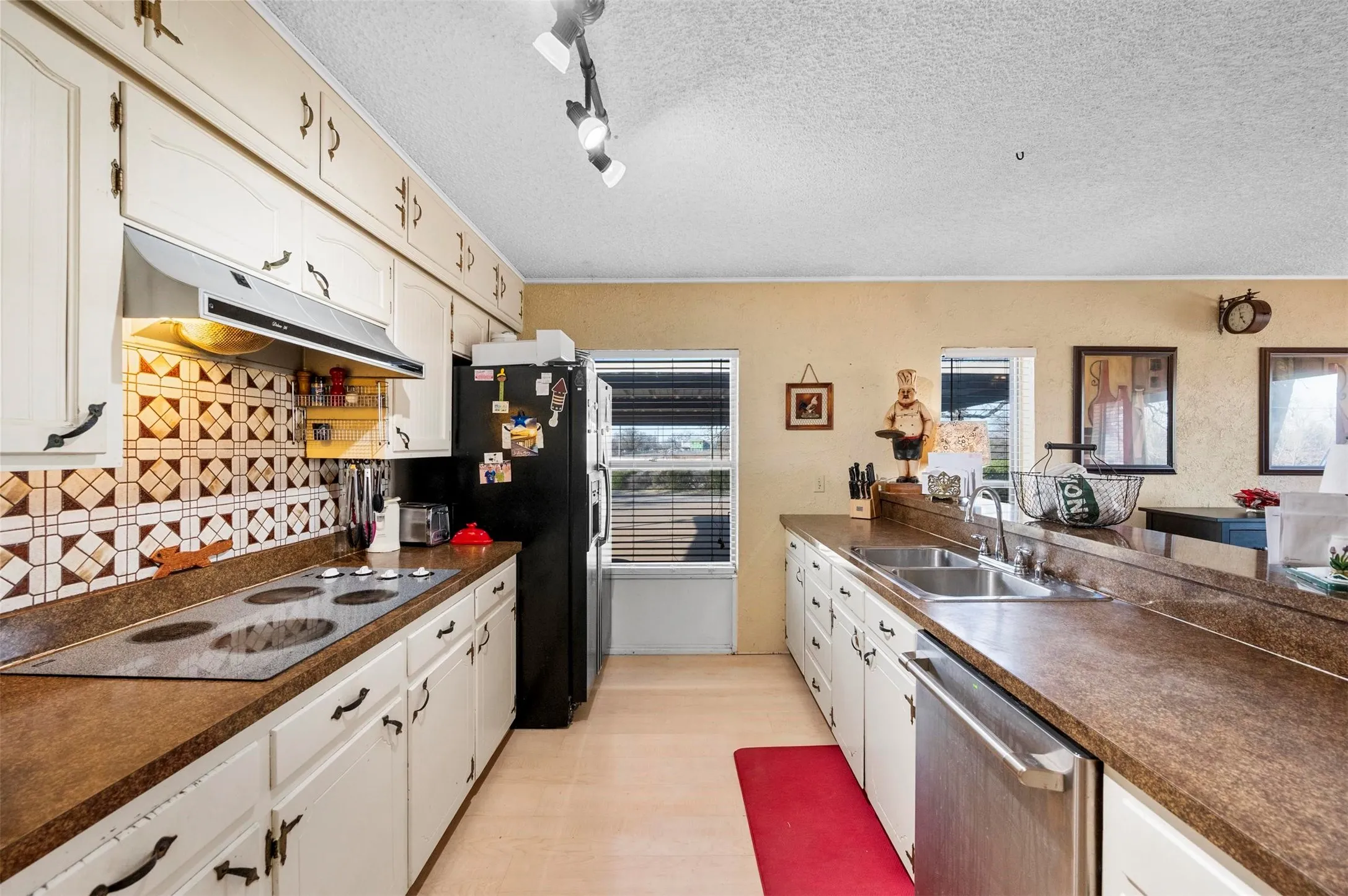Kitchen with a sink, dark countertops, electric cooktop, under cabinet range hood, and stainless steel dishwasher