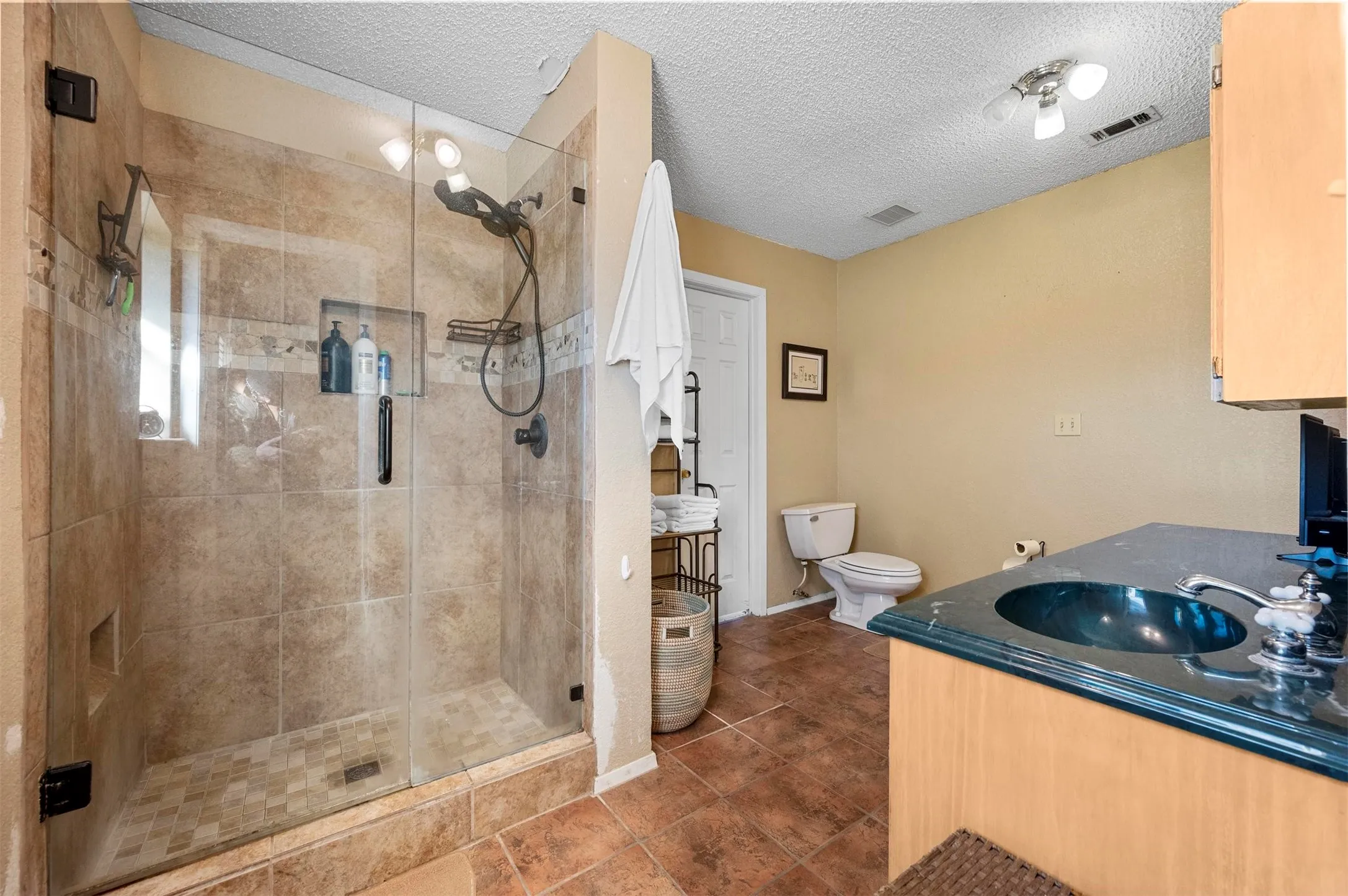 Full bathroom with visible vents, toilet, a textured ceiling, vanity, and a stall shower