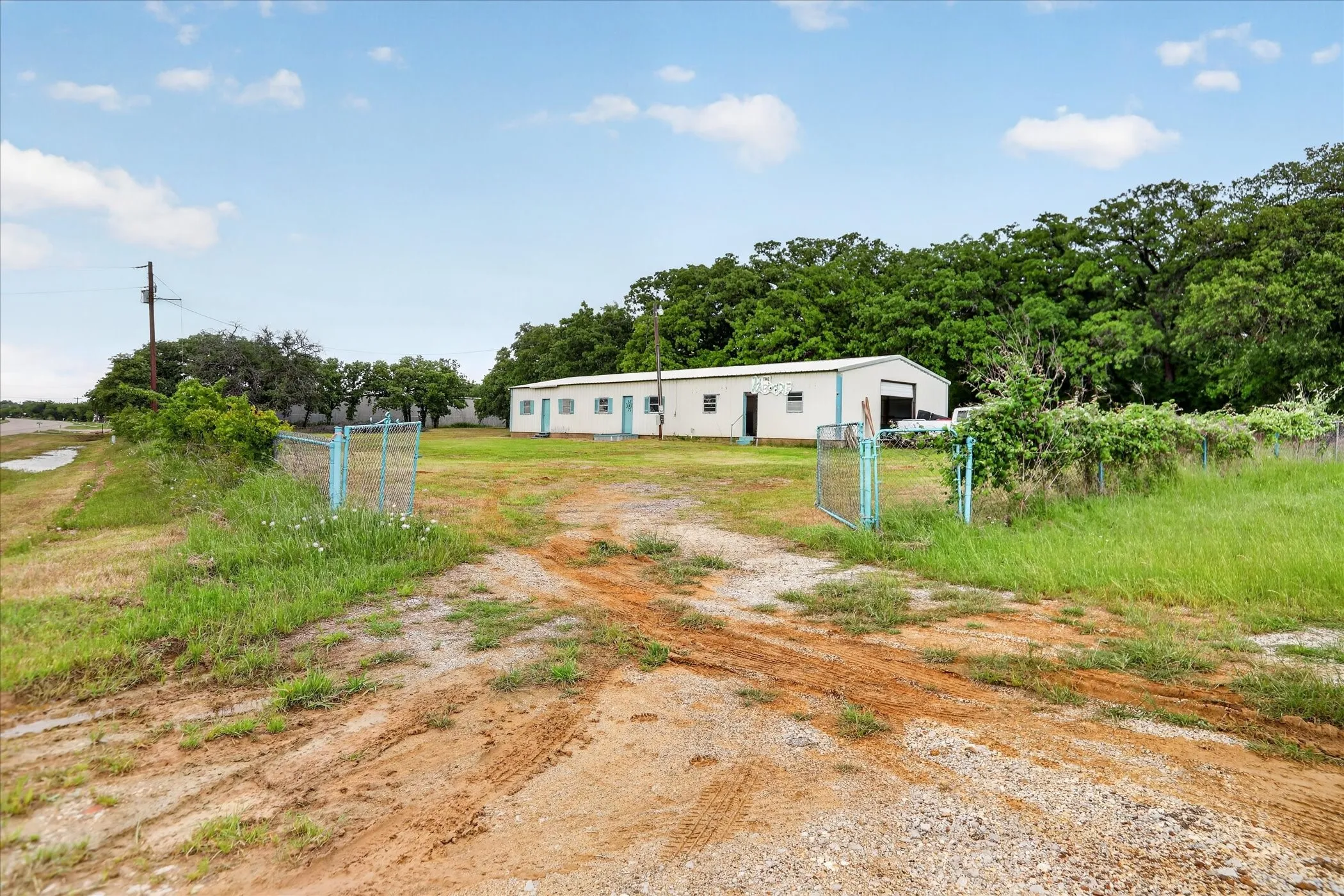 Large metal building with multiple entry points, featuring a gravel driveway and gated entry