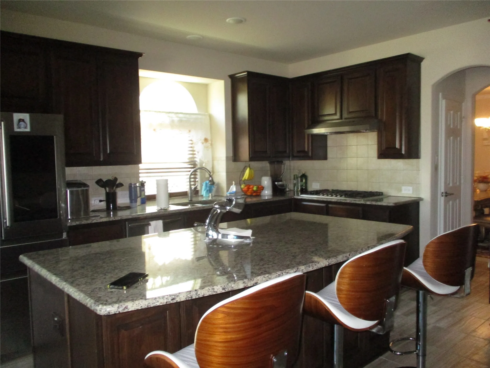 Kitchen with tasteful backsplash, arched walkways, light stone counters, and stainless steel gas stovetop
