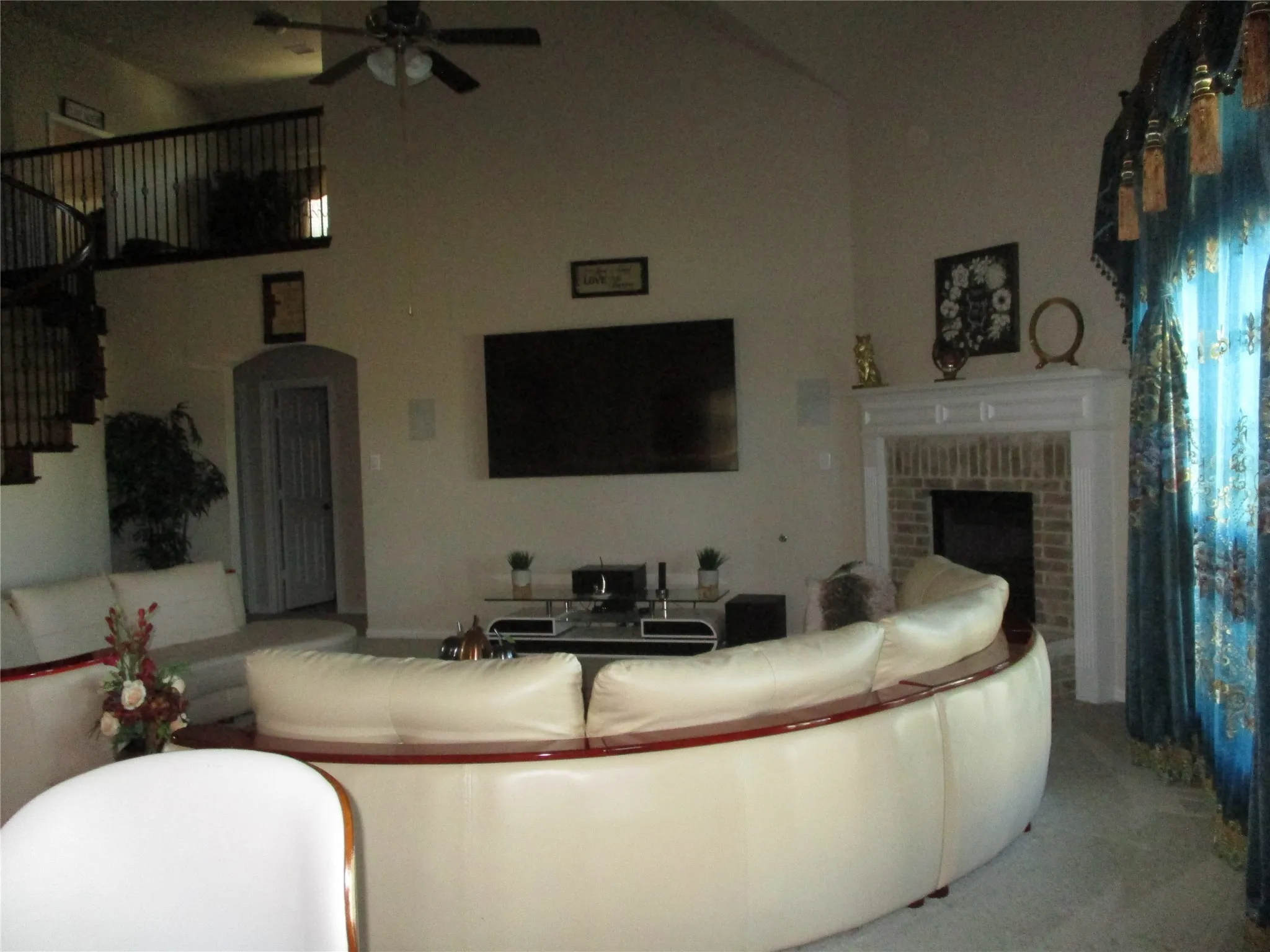 Living area with arched walkways, a fireplace, a ceiling fan, and stairs