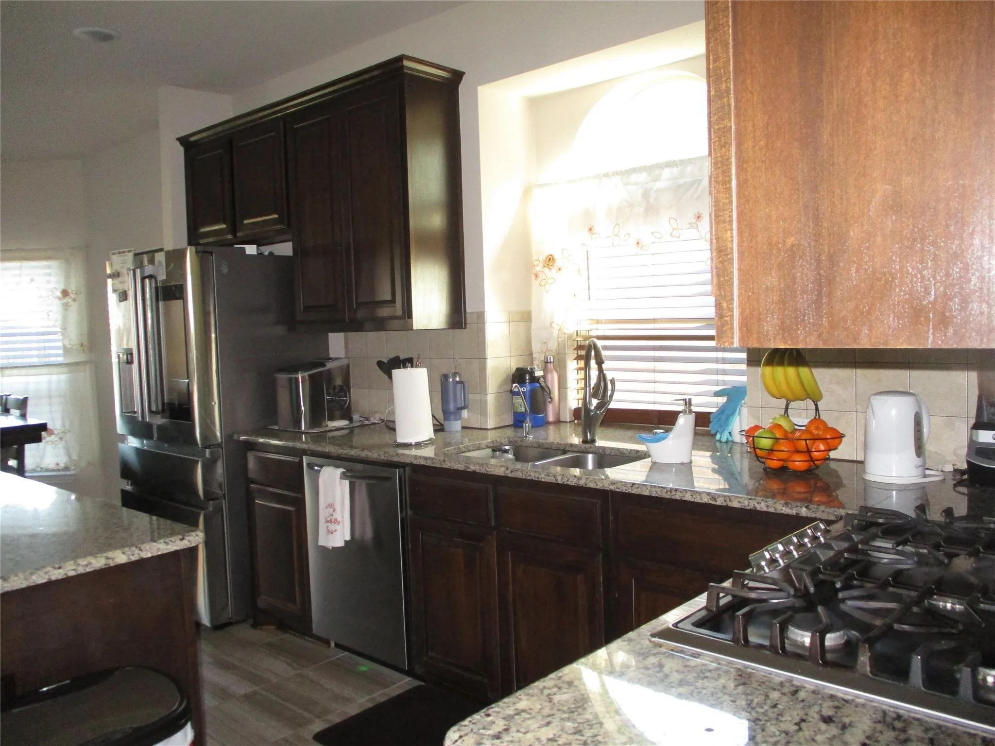 Kitchen with tasteful backsplash, a sink, dark brown cabinets, light stone countertops, and stainless steel appliances