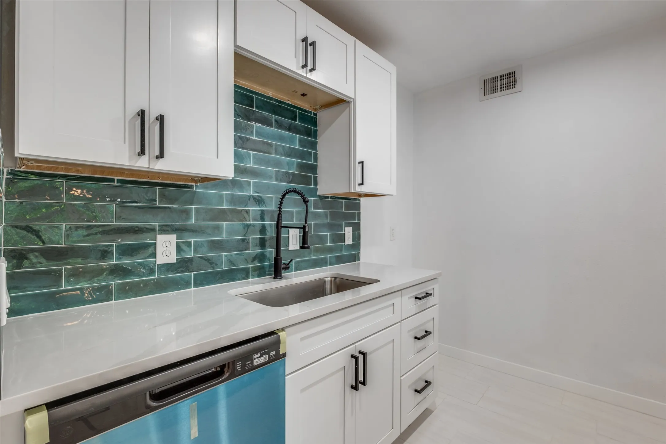 Kitchen with visible vents, baseboards, a sink, dishwashing machine, and decorative backsplash