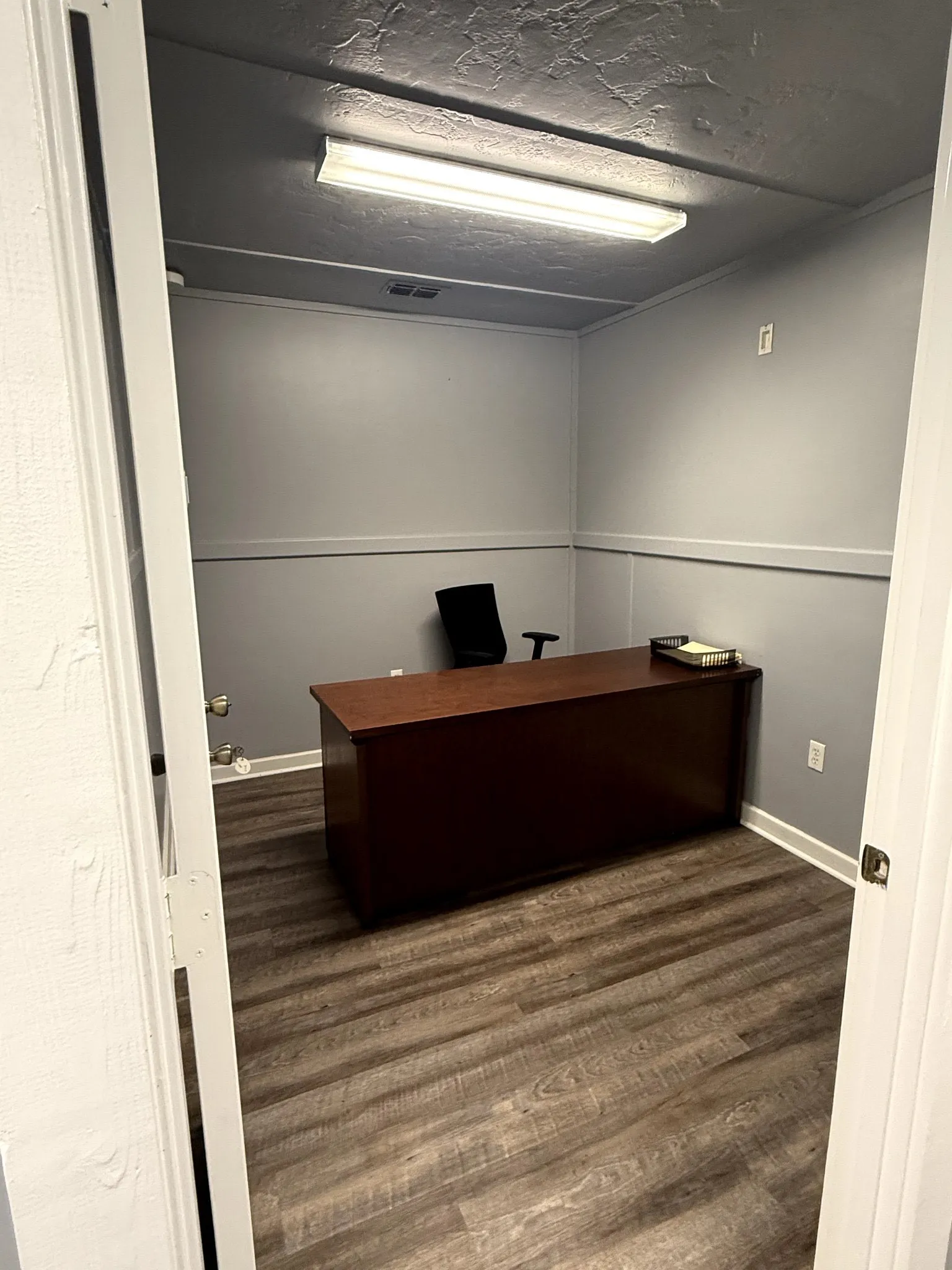 Wood-finish flooring with white trim, light gray walls, and overhead fluorescent lighting
