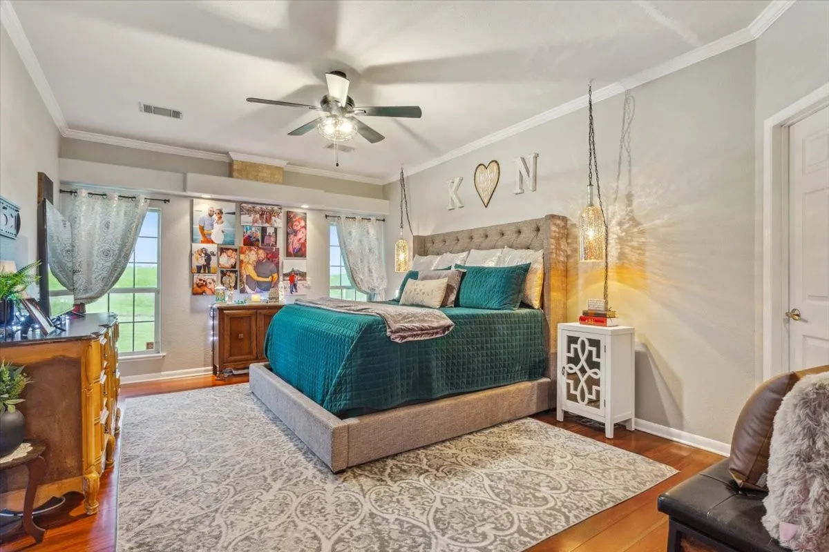 Bedroom featuring baseboards, wood finished floors, visible vents, and ornamental molding