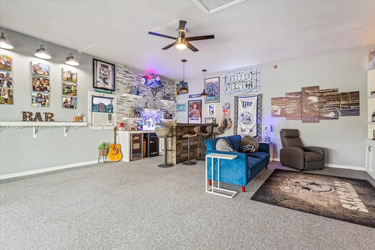 Carpeted living room with baseboards, a ceiling fan, and a bar
