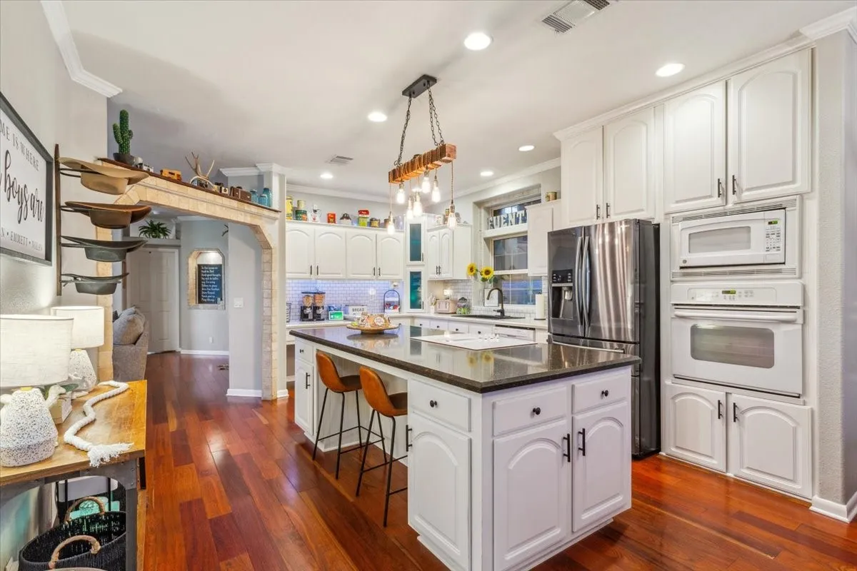Kitchen with white cabinets, a center island, dark countertops, visible vents, and white appliances