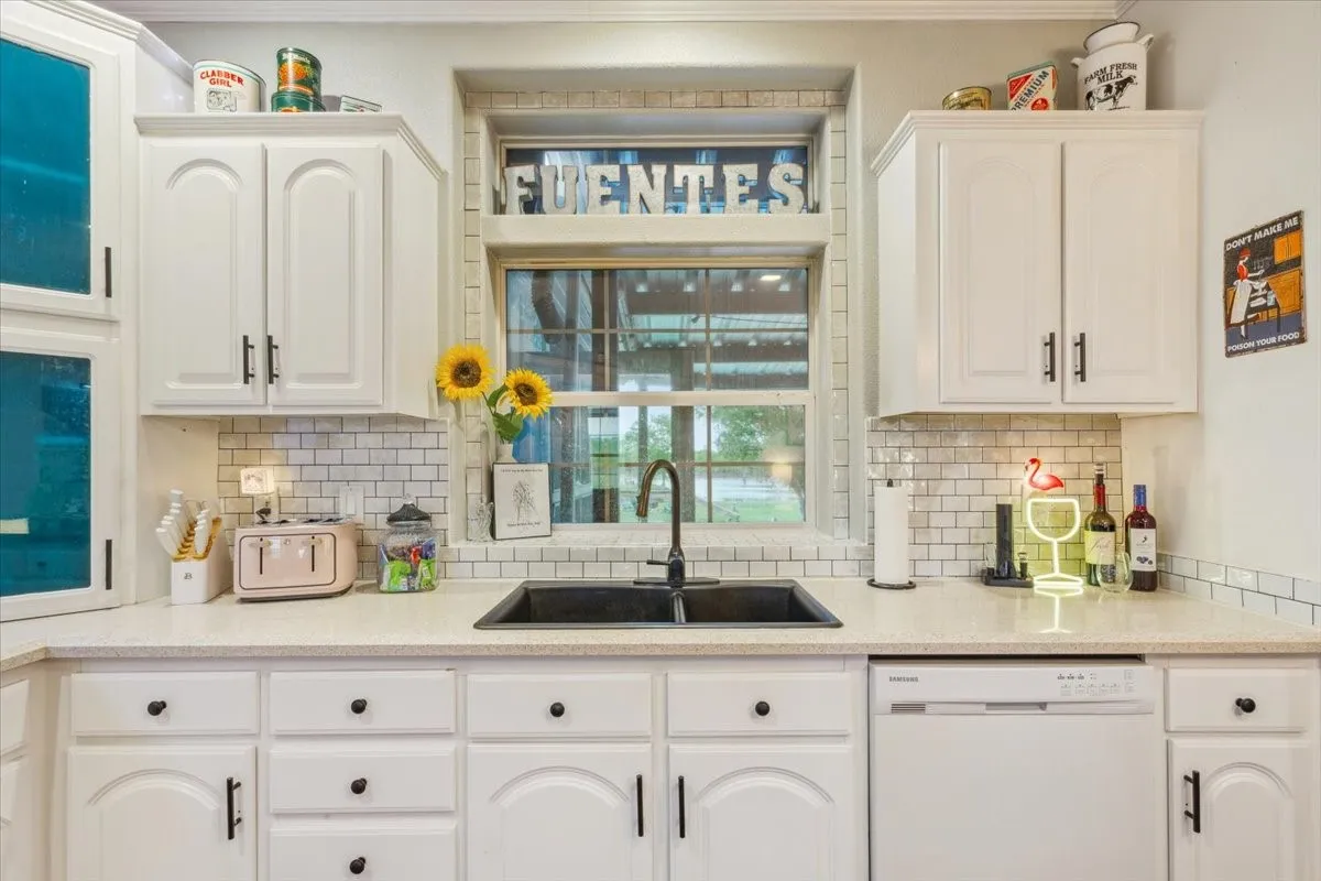 Kitchen with a sink, decorative backsplash, dishwasher, light countertops, and white cabinetry