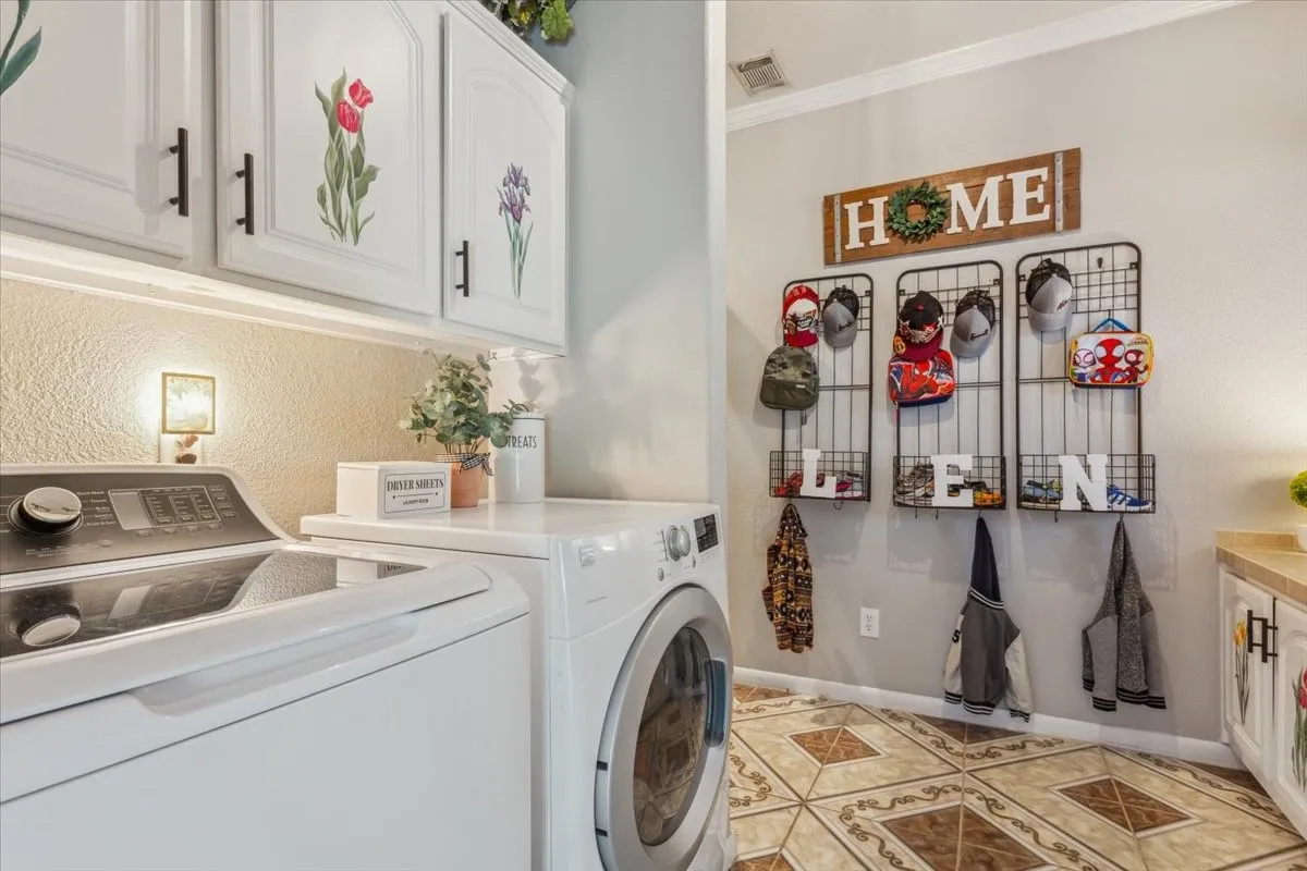 Laundry room featuring washing machine and clothes dryer, cabinet space, crown molding, and visible vents