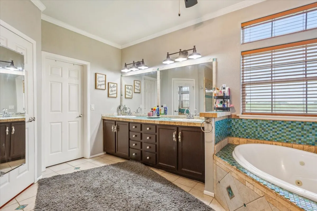 Bathroom with a jetted tub, a sink, tile patterned flooring, and ornamental molding