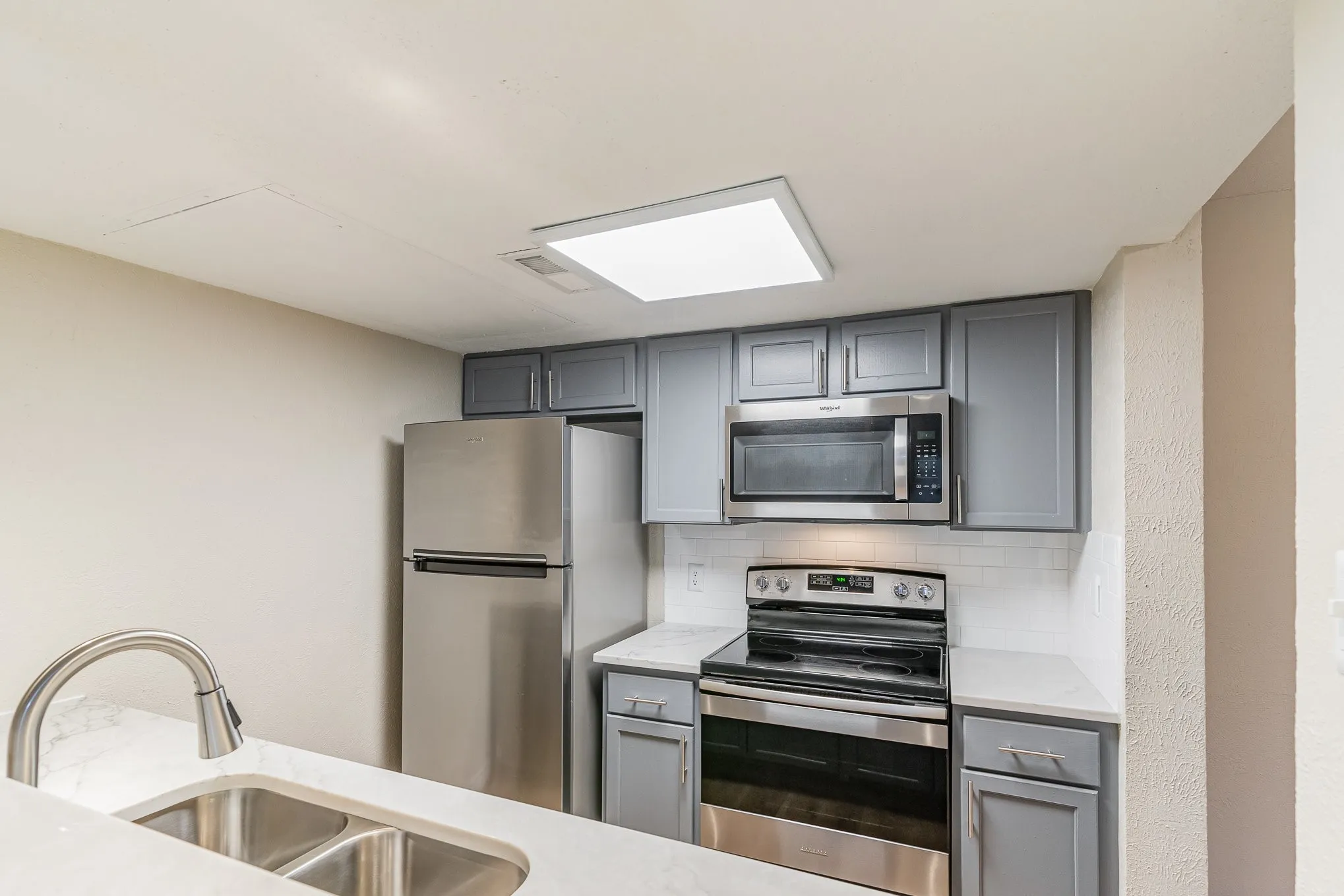 Kitchen featuring a sink, decorative backsplash, gray cabinetry, light countertops, and appliances with stainless steel finishes